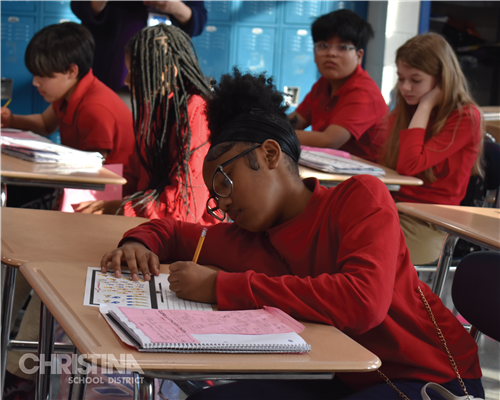 Female student working on assignment while other students work on an assignment